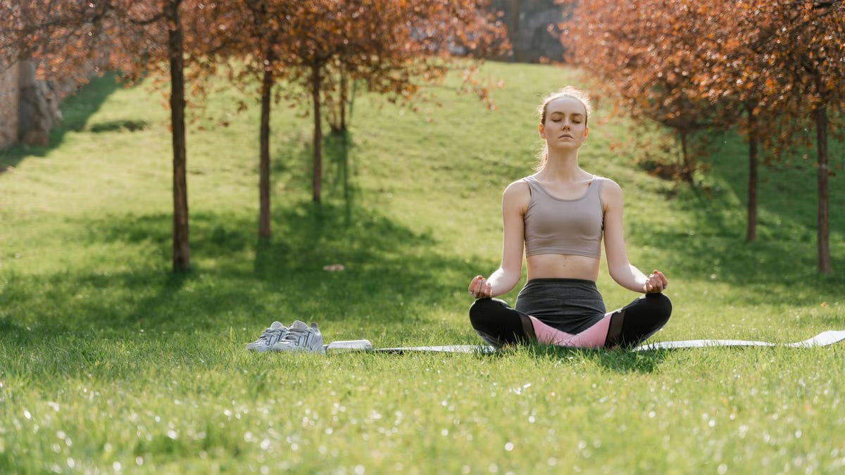 Woman practicing meditation in a sunny park, enhancing wellness and mindfulness.